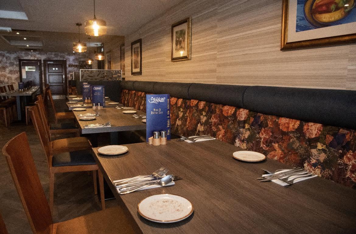 Inside the Qismat dining room: wooden tables laid for dinner along a floral banquette