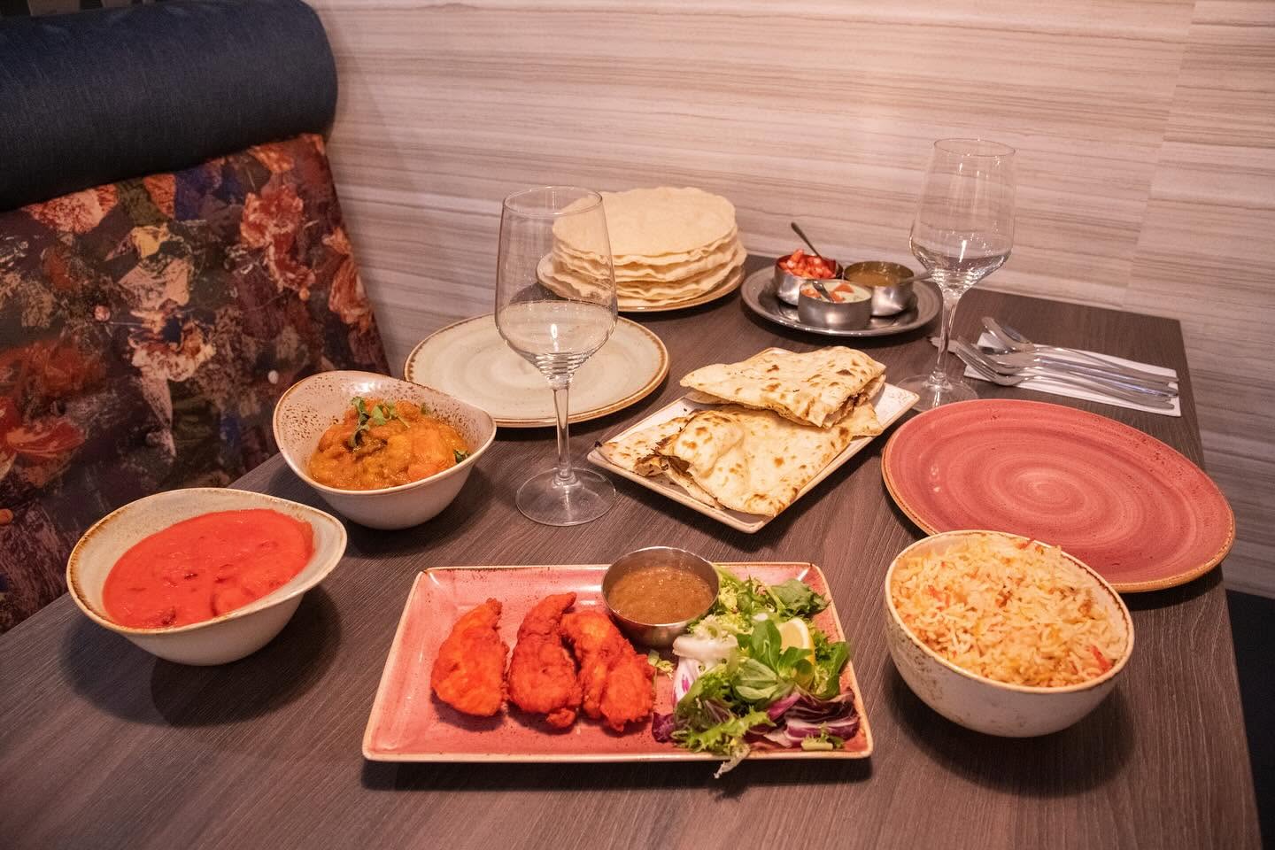 A table spread of curries, tandoori chicken, naan, pilau rice and poppadoms